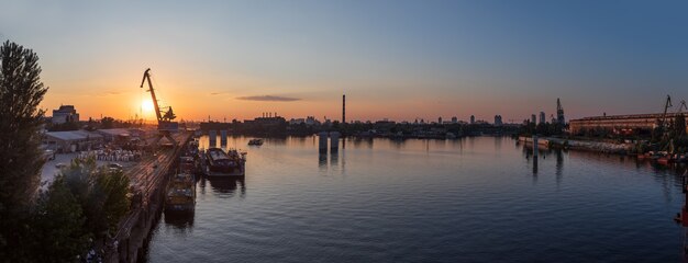 Kijów, Ukraina - 30 maja 2018: Przemysłowa dzielnica Kijowa w dzielnicy Podil. Dniepr i port rzeczny. Widok z mostu wantowego Rybalsky wieczorem podczas zachodu słońca