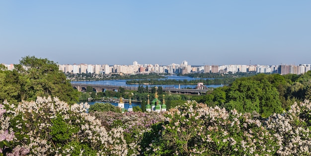 Kijowskie krajobrazy. Wiosenny widok klasztoru Vydubychi i rzeki Dnipro z różowym i białym bzem kwitnącym w ogrodzie botanicznym w mieście Kijów, Ukraina