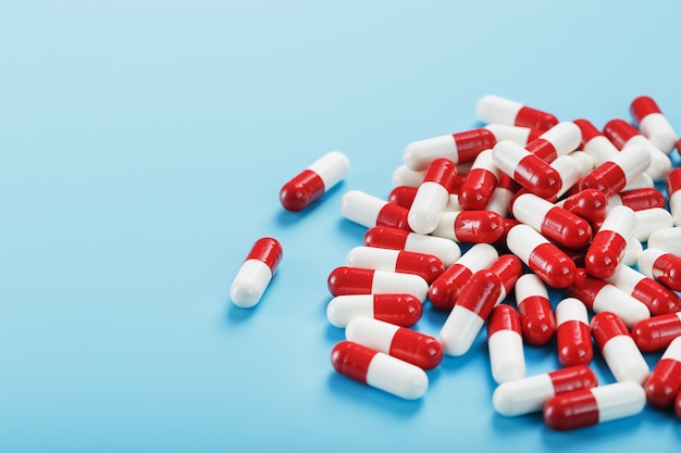 Kilka czerwonych i białych tabletek na niebieskim tle. Widok z góry