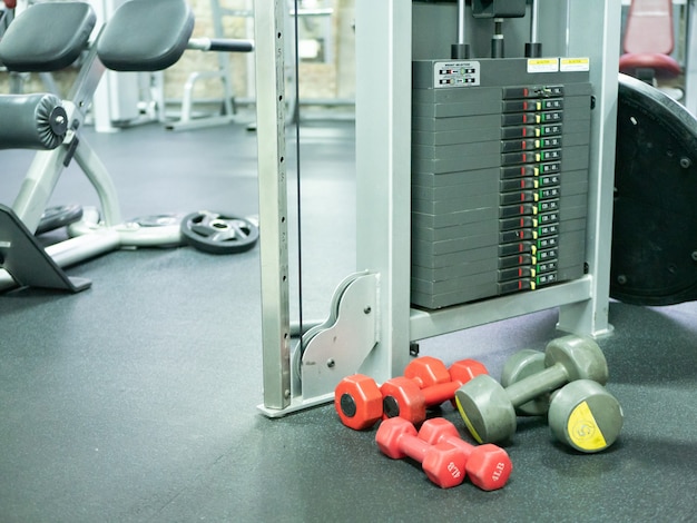 Zdjęcie kilka lekkich hantli na podłodze sali gimnastycznej w pobliżu maszyny do treningu crossowego o dużej wadze