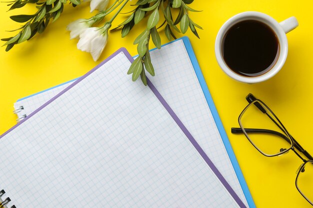 Kilka notebooków i szklanki filiżankę kawy i kwiaty na jasnożółtym tle. widok z góry. narzędzia biurowe