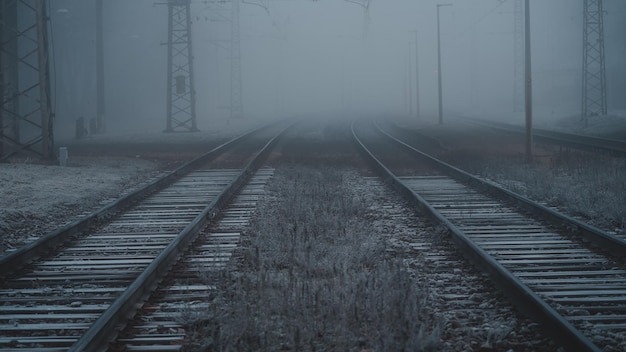 Kilka torów kolejowych kończących się we mgle, tory kolejowe w zimny jesienny poranek