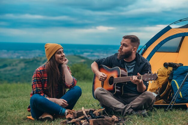 Kilku obozowiczów grających na gitarze i spędzających romantyczne chwile podczas biwakowania na łonie natury