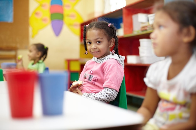 Zdjęcie klasa dla dzieci i lunch w portrecie z uśmiechem do edukacji przy stole z dziećmi przerwa dla dzieci i nauka w szkole z jabłkiem w przedszkolu z krzesłem lub biurkiem z jedzeniem z przyjaciółmi