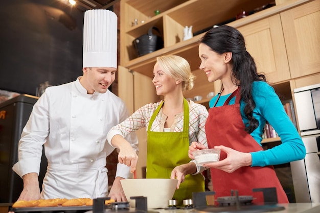 klasa gotowania, koncepcja kulinarna, piekarnicza, jedzenie i ludzie - szczęśliwa grupa kobiet i kucharzy kucharzy kucharzy pieczenia babeczek w kuchni