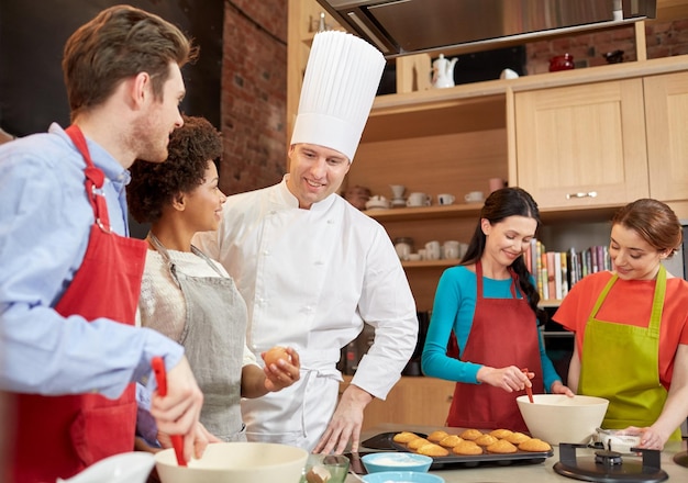 Zdjęcie klasa gotowania, koncepcja kulinarna, piekarnicza, jedzenie i ludzie - szczęśliwa grupa przyjaciół i kucharz kucharz kucharz w kuchni
