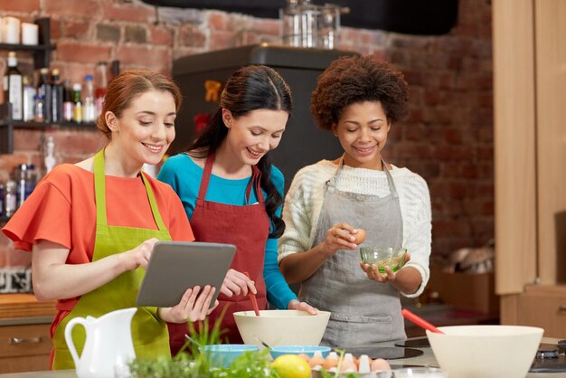 klasa gotowania, przyjaźń, jedzenie, technologia i koncepcja ludzi - szczęśliwe kobiety z komputerem typu tablet w kuchni