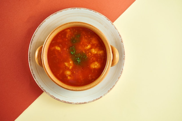 Klasyczna belgijska czerwona zupa z pomidorami i małymi klopsikami w glinianym talerzu na kolorowej powierzchni.