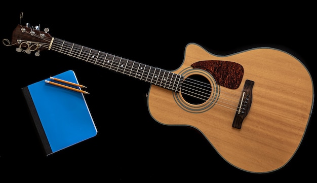 Klasyczna gitara akustyczna i niebieski notatnik na czarnym tle, widok z góry, koncepcja kreatywności muzycznej.