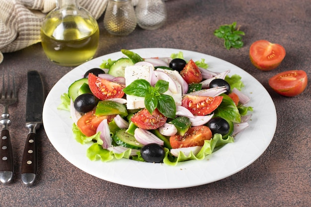 Klasyczna grecka sałatka z pomidorów, ogórków, słodkiej papryki, oliwek, bazylii i sera feta na białym talerzu