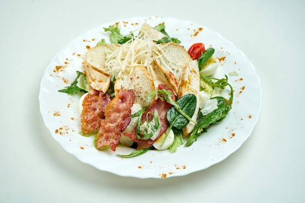 Klasyczna sałatka Cezar z sałatą, szpinakiem, kurczakiem, grzankami, parmezanem i boczkiem w białym talerzu na białym talerzu