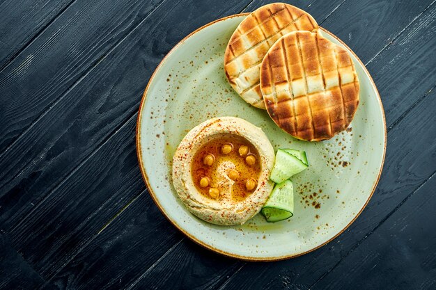 Klasyczne danie orientalne - hummus z oliwą i ciecierzycą podany z pitą pieczoną w talerzu na powierzchni z ciemnego drewna. Jedzenie wegetariańskie. Dieta