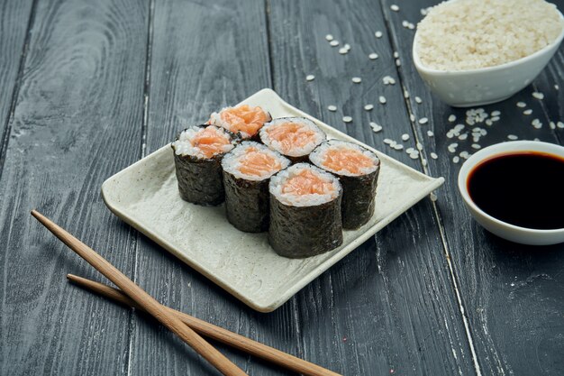 Klasyczne japońskie sushi rolki - maki rolki z łososiem na białym, ceramicznym talerzu na czarnym drewnianym tle