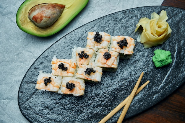 Zdjęcie klasyczne japońskie sushi z krewetkami, krabem i kawiorem. california roll na czarnej płycie pałeczkami. kuchnia japońska. zdrowe owoce morza