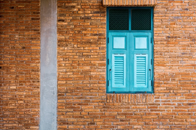 Klasyczne okno z zielonego i niebieskiego drewna w zabytkowym budynku z cegły.
