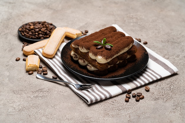 Klasyczny deser tiramisu i ciasteczka savoiardi na talerzu ceramicznym na betonowym stole