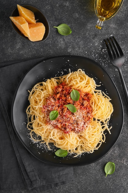 Klasyczny makaron spaghetti Bolognese Smaczne apetyczne włoskie spaghetti z sosem bolońskim sos pomidorowy ser parmezan i bazylia na czarnym talerzu na ciemnym kamiennym lub betonowym tle stołu Widok z góry