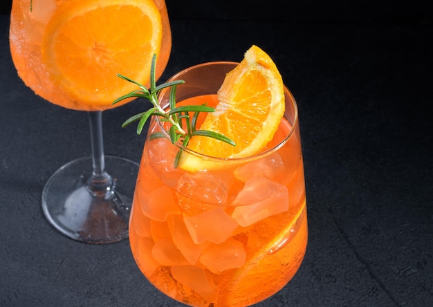 Klasyczny włoski aperitif aperol spritz koktajl w dwóch szklankach z lodową pomarańczą na czarnym tle z bliska