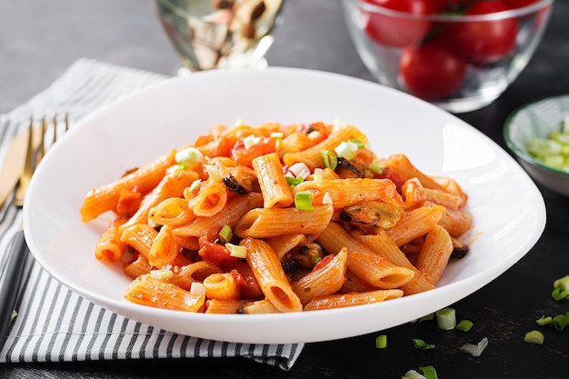 Klasyczny włoski makaron penne marinara z małżami i zieloną cebulką na ciemnym stole. Makaron penne z sosem marinara.