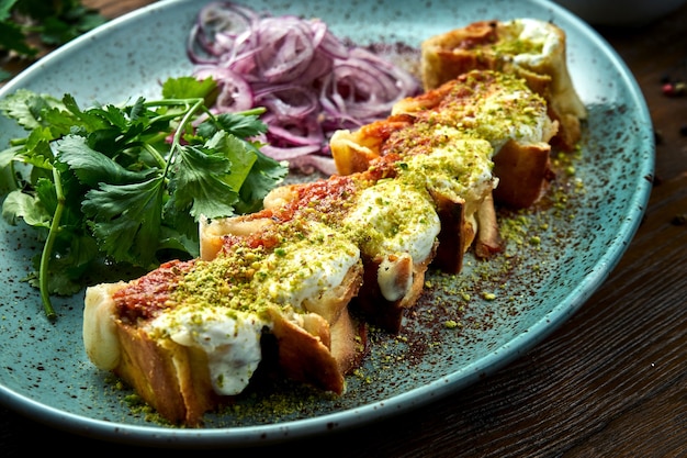 Klasycznym tureckim daniem jest shawarma w plastrach z kebabem drobiowym polanym czerwono-białym sosem pistacjowym, podawana na niebieskim talerzu na drewnianym stole. Jedzenie w restauracji