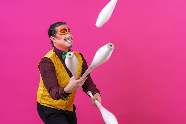 Klaun z białym makijażem twarzy na różowym tle żonglerka maczugami