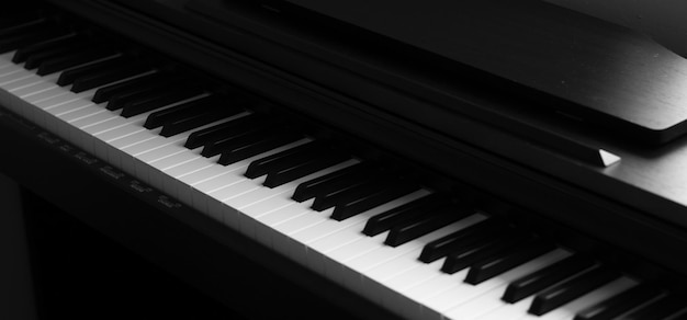 Klawiatura fortepianu i pianina elektronicznego z czarnym tłem. Zbliżenie czarno-białe klawisze fortepianu, miejsce na kopię, baner