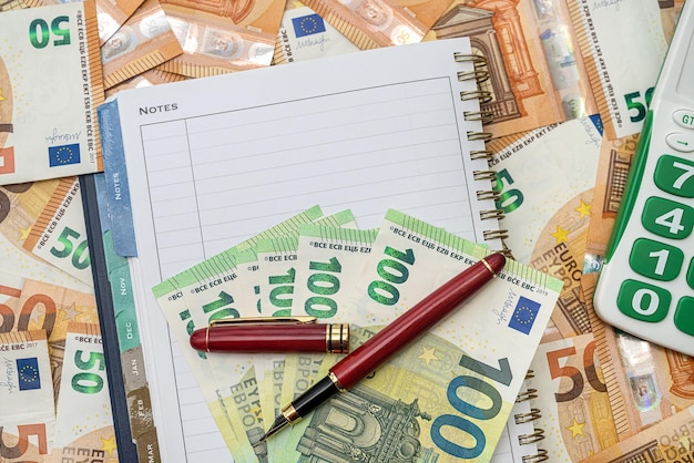 Klawiatura kalkulatora zielony czysty nowy notatnik i czerwony długopis stoją na nowych banknotach euro. Koncepcja pieniądza biznesowego