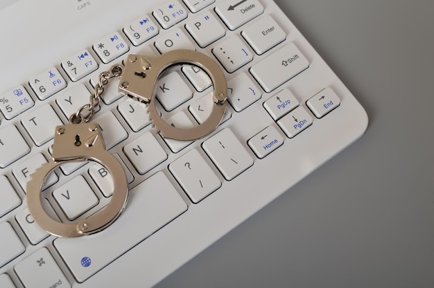 Klawiatura laptopa i kajdanki izolowane na szarym tle Skopiuj miejsce na tekst Oszustwo online, oszustwo, oszustwo, aresztowanie i koncepcja karna