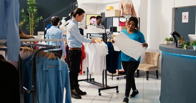 Klient potrzebował pomocy z modnymi koszulami, omawiając materiał z azjatyckim pracownikiem w nowoczesnym butiku. Afroamerykanka kupuje stylowe ubrania w sklepie odzieżowym
