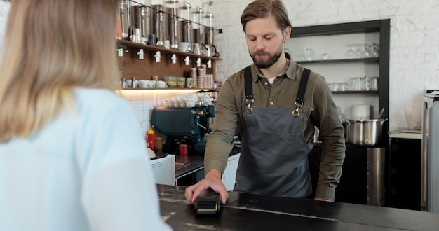 Klientka płaci za kawę na wynos dzięki technologii płatności zbliżeniowych NFC na smartfonie