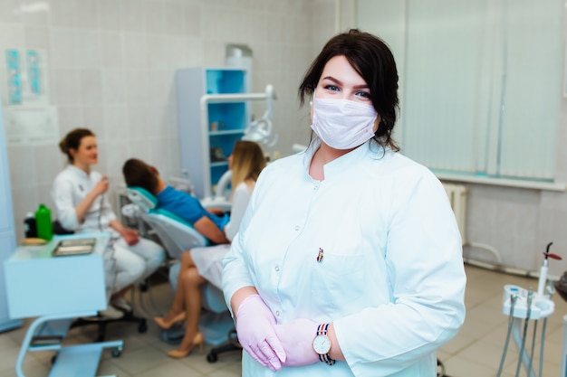 Klinika Dentystyczna. Portret Profesjonalnego Dentysty Na Tle Pracującego Zespołu Lekarzy. Pojęcie Edukacji Medycznej I Ubezpieczenia Medycznego.