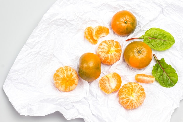 Zdjęcie kliny mandarynki i cała mandarynka, liście boćwiny na białym papierze. białe tło. leżał na płasko. skopiuj miejsce