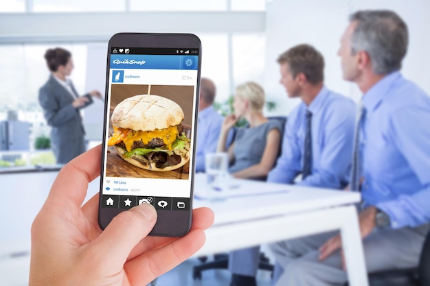 Zdjęcie kobieca dłoń trzymająca smartfon przed zbliżeniem na serowego burgera i frytki