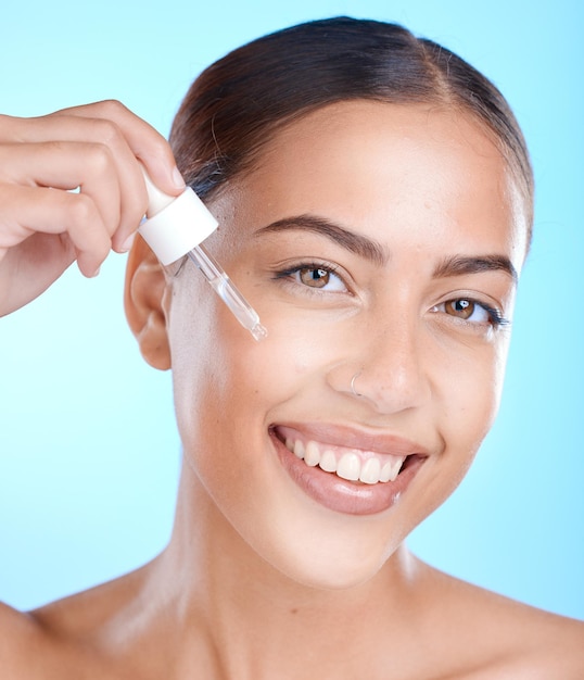 Kobieca pielęgnacja twarzy i serum w studio na niebieskim tle w celu promowania produktu kosmetycznego Uśmiech na twarzy i przeciwdziałanie starzeniu z szczęśliwą kobietą nakładającą olej na skórę w celu naturalnej kosmetologii