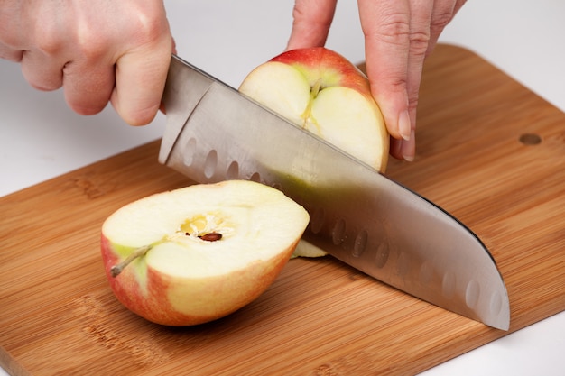 Kobieca ręka kuchennym nożem przecięła duże czerwone jabłko na pół na drewnianej desce