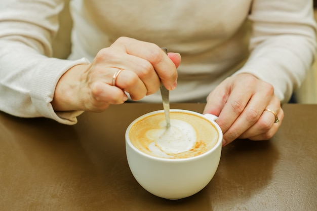 Kobieca ręka mieszając filiżankę kawy. Rano świeżo ugotowane cappuccino