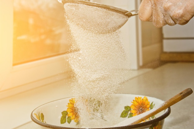 Kobieca ręka przesiewająca mąkę przez ręczne sito do mąki w misce zbliżenie kopia przestrzeń gotowanie ciasta metalowe urządzenie kuchenne