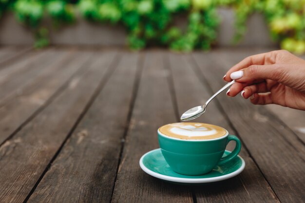 Kobieca ręka trzymająca łyżkę nad świeżo zaparzonym aromatem cappuccino w pięknej turkusowej filiżance