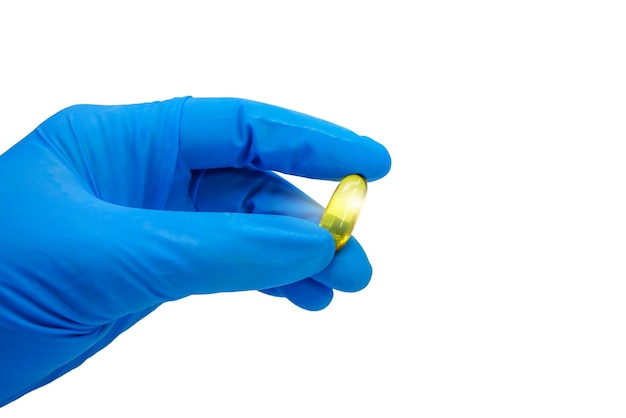 Kobieca ręka w niebieskich rękawiczkach medycznych trzymająca tabletki oleju z wątroby dorsza na białym tle