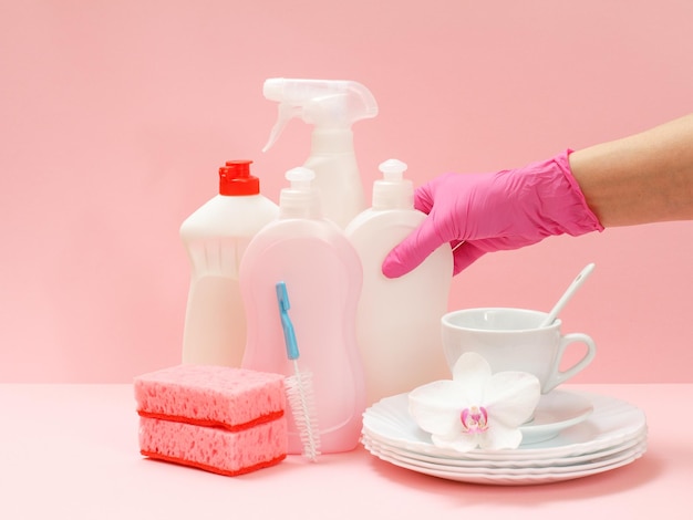 Kobieca ręka w nitrylowej rękawiczce z butelką płynu do mycia naczyń na różowym tle