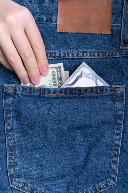 Kobieca ręka wkłada 100-dolarowy banknot i prezerwatywę do tylnej kieszeni dżinsów