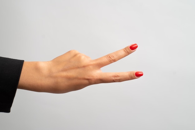 Kobieca ręka z czerwonym manicure pokazuje gest na białym tle