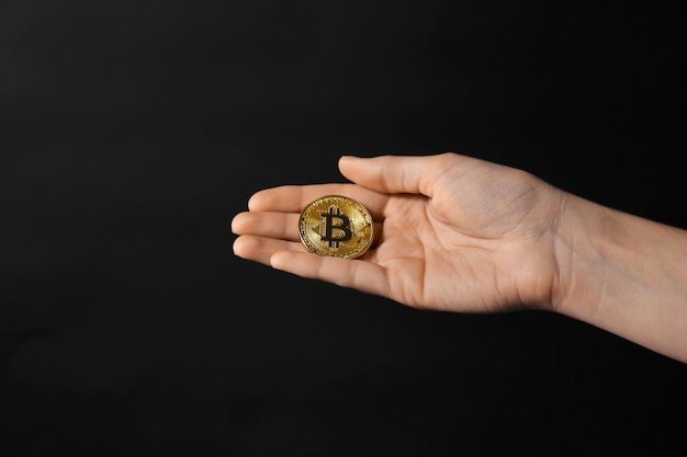 Kobieca ręka ze złotym bitcoinem na ciemnym tle