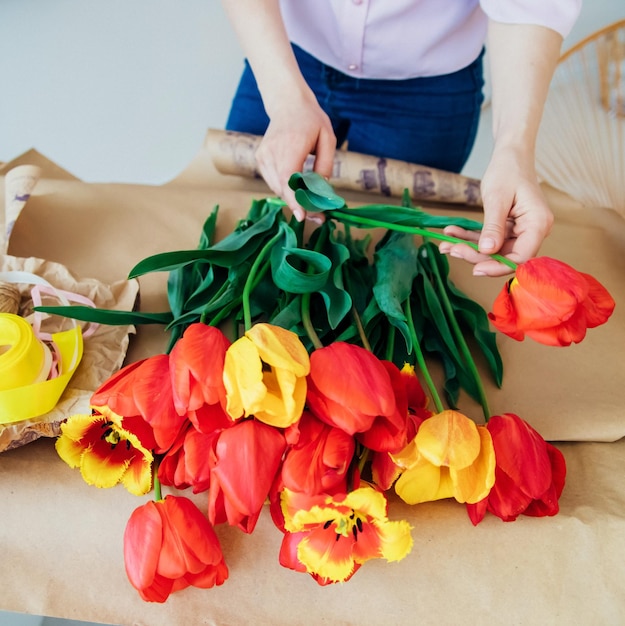 Zdjęcie kobiece dłonie pakują świąteczny bukiet w papier pakowy kwiaciarnia składa apel z czerwonymi tulipanami w warsztacie kobieta przy pracy mały biznes lub hobby