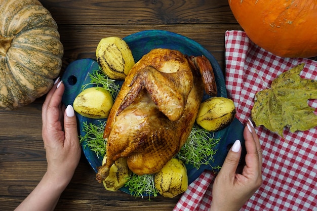 Kobiece dłonie podają na stół świeżo ugotowanego kurczaka z ziemniakami i mikro zielenią