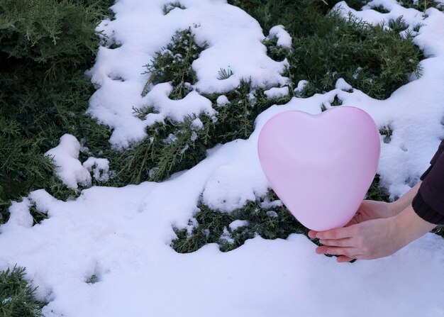 kobiece dłonie trzymają różowy balon w kształcie serca zimą na zewnątrz w pobliżu zaspy śnieżnej