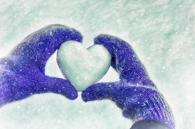 kobiece dłonie w dzianinowych rękawiczkach z sercem śniegu w zimowy dzień. Koncepcja miłości. Walentynki tło