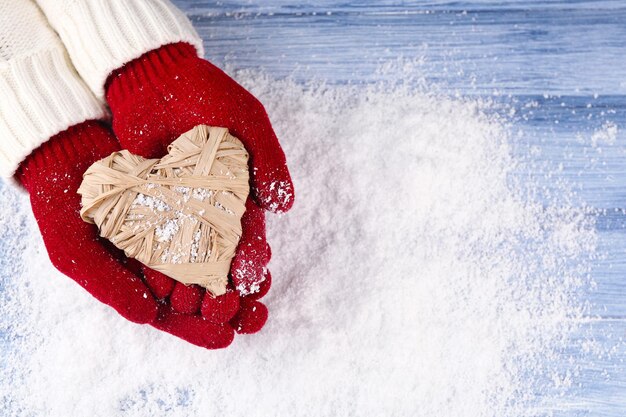 Kobiece dłonie w rękawiczkach z ozdobnym sercem na tle śniegu