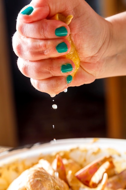 Kobiece dłonie wyciskają sok z cytryny na skrzydełka kurczaka w przyprawach