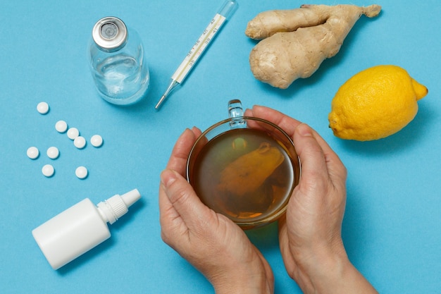 Kobiece dłonie z filiżanką herbaty i produkty lecznicze na przeziębienie i grypę